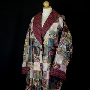May include: A long-sleeved jacket featuring a patchwork design of various floral and abstract patterns in shades of burgundy, blue, and cream. The garment has a wide burgundy collar with a small white dot pattern, matching cuffs, and two buttons.