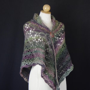 Peut inclure: Un châle au crochet présentant un motif de fil panaché dans des tons de vert forêt, violet profond et gris anthracite. Le vêtement présente un design en maille ajourée et est attaché sur le devant par un seul bouton en bois rond brun-rouge.