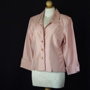 May include: A light pink blazer with a collared neckline, three front buttons, and three-quarter length sleeves featuring folded cuffs. The garment has a smooth, slightly lustrous finish and is displayed on a white mannequin torso.