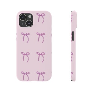 May include: A pink phone case with a pattern of purple bows. The case is designed for a phone with a camera bump.