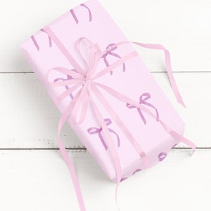 May include: A pink gift box with a pink ribbon tied in a bow. The box is decorated with a pattern of pink bows.