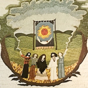 May include: Embroidered artwork depicting five figures standing in a circle around a banner with a sun and moon design. The figures are wearing long, flowing robes and have long hair. The background is a green field with a tree on either side.