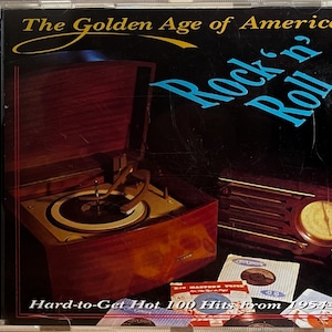 May include: A vintage-style record player with a wooden cabinet and a turntable. The record player is playing a record. The image also shows a vintage radio with a dial and a speaker. The text on the image reads "The Golden Age of American Rock 'n' Roll Hard-to-Get Hot 100 Hits From 1954-63".