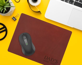 May include: A brown leather mouse pad with the text "DAD'S HOME OFFICE" in a white font. A black wireless mouse is on the mouse pad.