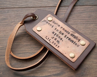 May include: A brown leather luggage tag with a copper plate that reads "Some roads aren't meant to be traveled alone. J & K. 5.11.2015".