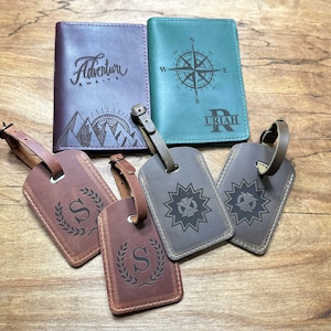 Puede incluir: Dos fundas rectangulares para pasaporte y cuatro etiquetas de equipaje. Una funda morada presenta un gr&aacute;fico de monta&ntilde;as y el texto Adventure Awaits. Una funda verde azulado muestra una br&uacute;jula y el nombre URIAH. Cuatro etiquetas tienen letras y estrellas grabadas.