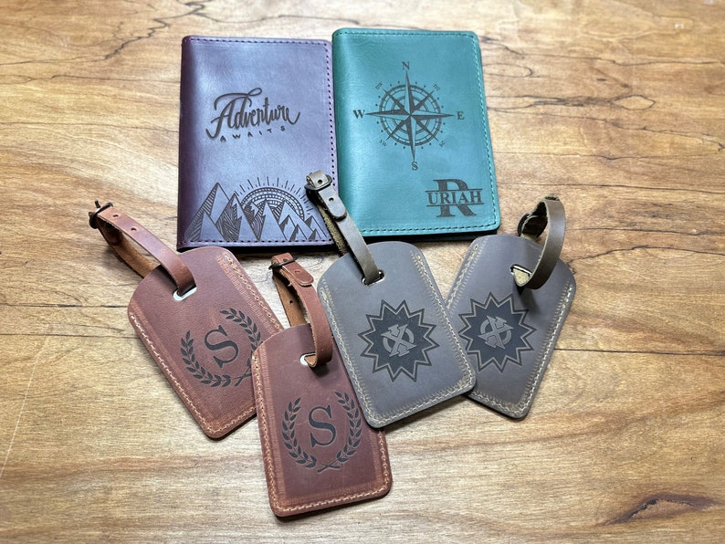 Puede incluir: Dos fundas rectangulares para pasaporte y cuatro etiquetas de equipaje. Una funda morada presenta un gr&aacute;fico de monta&ntilde;as y el texto Adventure Awaits. Una funda verde azulado muestra una br&uacute;jula y el nombre URIAH. Cuatro etiquetas tienen letras y estrellas grabadas.