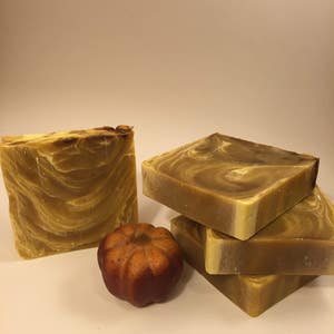 May include: Four bars of handmade soap with a swirl pattern in shades of brown and yellow. A small orange pumpkin sits in front of the soap bars.