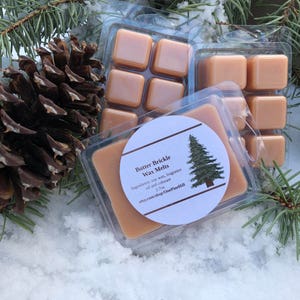 May include: Six brown wax melts in a clear plastic container. The container has a white label with the text "Butter Brickle Wax Melts" and "Ingredients: soy wax, fragrance oil and colorant 2.7oz etsy.com/shop/OnePineHill".