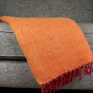 May include: A soft, orange throw blanket with a red fringe. The blanket is draped over a grey sofa.