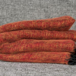 Peut inclure: Une couverture en laine orange et rouge pliée avec des franges noires.