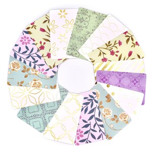 Peut inclure: Un ensemble de 12 cartes d&eacute;coratives avec diff&eacute;rents motifs floraux et g&eacute;om&eacute;triques dans des tons de vert, de violet et d'or. Les cartes sont dispos&eacute;es en cercle, les accents dor&eacute;s &eacute;tant tourn&eacute;s vers l'ext&eacute;rieur.
