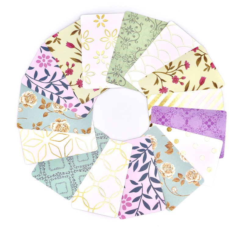 Peut inclure: Un ensemble de 12 cartes d&eacute;coratives avec diff&eacute;rents motifs floraux et g&eacute;om&eacute;triques dans des tons de vert, de violet et d'or. Les cartes sont dispos&eacute;es en cercle, les accents dor&eacute;s &eacute;tant tourn&eacute;s vers l'ext&eacute;rieur.