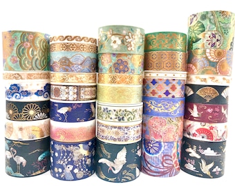 May include: A collection of twenty-five rolls of decorative washi tape stacked in five columns. The tapes feature various patterns including cranes, fans, floral motifs, and geometric designs in gold, blue, green, pink, and black colors.