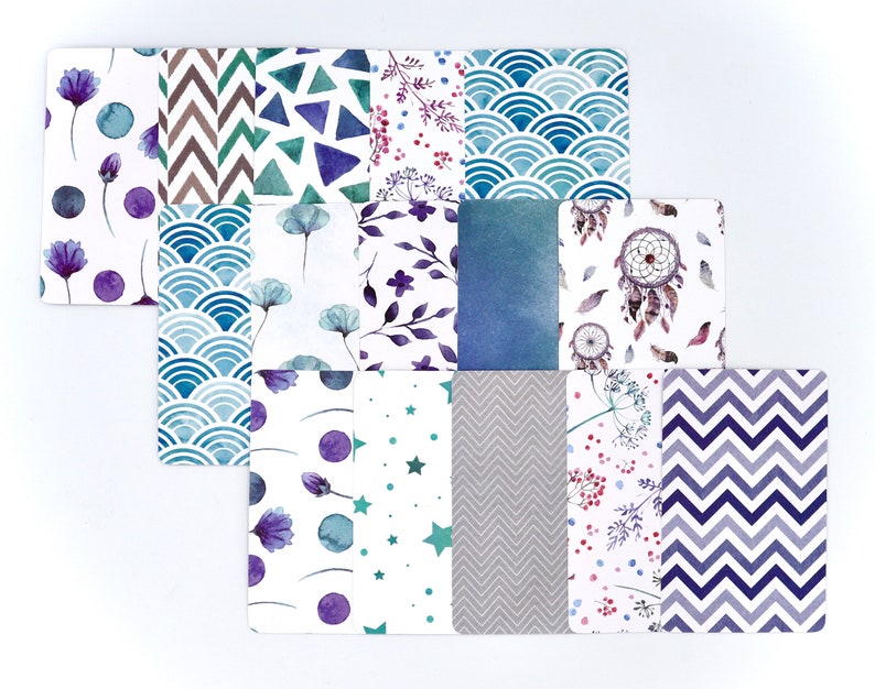 Peut inclure: Un ensemble de 12 papiers num&eacute;riques avec diff&eacute;rents motifs, y compris des formes g&eacute;om&eacute;triques, des motifs floraux et des attrape-r&ecirc;ves. Les motifs sont dans des tons de bleu, violet, vert et gris.