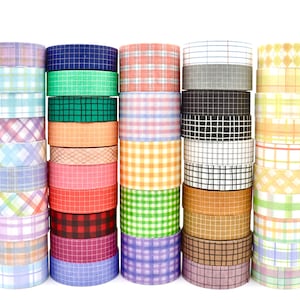 Peut inclure: Une collection de cinquante rouleaux de ruban adhésif washi disposés en cinq piles verticales. Chaque rouleau présente un motif distinct, incluant divers carreaux, vichy et quadrillages dans une large gamme de couleurs comme le bleu, le vert, l'orange, le rouge et le violet.
