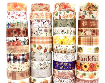 Può includere: Quattro pile verticali di rotoli di nastro adesivo decorativo washi con motivi a tema autunnale tra cui zucche, girasoli, funghi, foglie autunnali, stampe a quadri e la parola thankful stampata in un carattere corsivo marrone.
