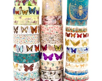 May include: Three vertical stacks of decorative washi tape rolls featuring various butterfly, floral, and bee motifs. The designs include colourful butterfly patterns, gold foil accents, and botanical illustrations on diverse backgrounds of blue, pink, and cream.