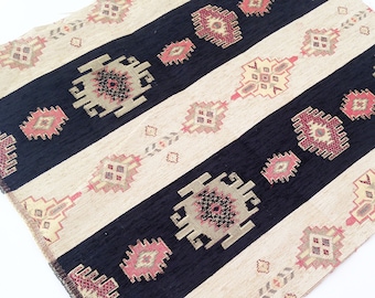 May include: A rectangular textile featuring alternating wide stripes of black and cream. The fabric is decorated with repeating geometric motifs in shades of pink, beige, and dark gray, arranged in a symmetrical pattern across the entire surface.