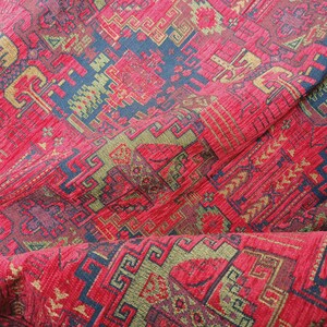 May include: Red, gold, and blue patterned fabric with a textured surface. The fabric has a geometric design with repeating patterns.