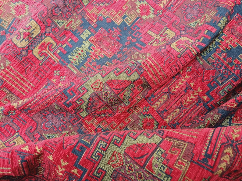 May include: Red, gold, and blue patterned fabric with a textured surface. The fabric has a geometric design with repeating patterns.