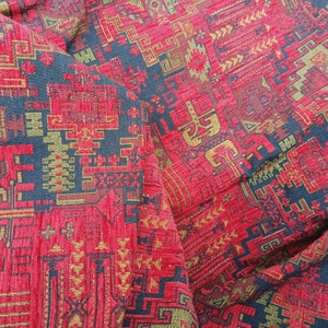 May include: Red fabric with a geometric pattern in gold and black. The fabric has a textured surface and a woven look.