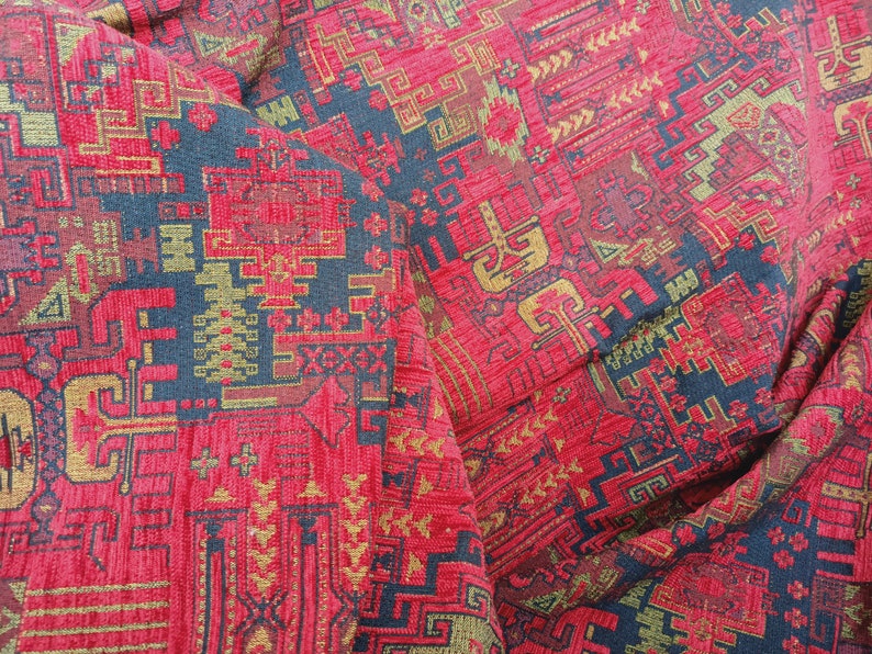 May include: Red fabric with a geometric pattern in gold and black. The fabric has a textured surface and a woven look.