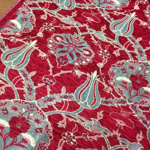 May include: Red fabric with a repeating pattern of stylized flowers and leaves in shades of gray and cream.