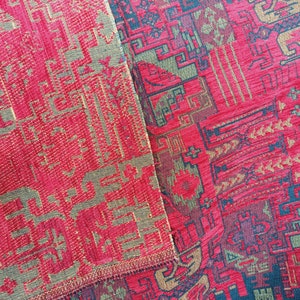 May include: Close-up of a red and gold patterned fabric with a geometric design. The fabric has a woven texture and a slightly raised pattern.