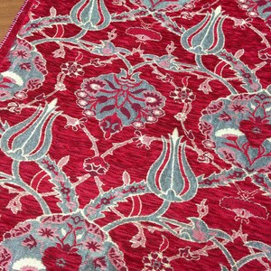 May include: Red fabric with a repeating pattern of gray and white stylized flowers and tulips. The fabric has a textured surface.