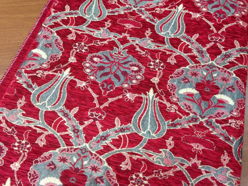 May include: Red fabric with a repeating pattern of gray and white stylized flowers and tulips. The fabric has a textured surface.