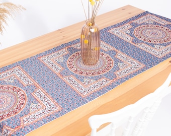 Könnte beinhalten: Ein rechteckiger Tischläufer mit blauem Hintergrund, dichtem Blumenmuster und sich wiederholenden geometrischen Motiven. Das Design umfasst große kreisförmige Medaillons in Rot-, Weiß- und Schwarztönen, die von komplexen weißen und roten Rändern umrahmt sind.