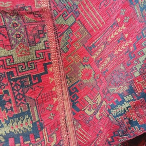May include: Close-up of a red, gold and black patterned fabric with a geometric design. The fabric has a textured surface and is woven with intricate details.