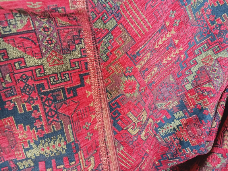 May include: Close-up of a red, gold and black patterned fabric with a geometric design. The fabric has a textured surface and is woven with intricate details.