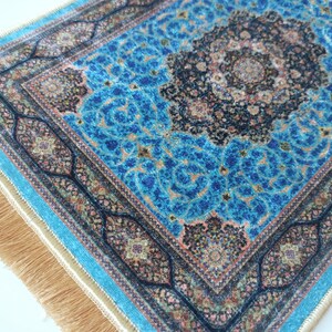 K&ouml;nnte beinhalten: Ein rechteckiger Teppich mit einem leuchtend blauen Hintergrund und komplizierten schwarzen und goldenen Blumenmustern. Der Teppich hat ein zentrales Medaillon-Design, einen detaillierten Rand und lange, hellbraune Fransen an den kurzen Kanten.