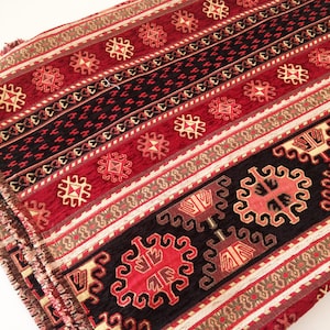 Puede incluir: Tela estampada en rojo, negro y dorado con un dise&ntilde;o geom&eacute;trico. La tela tiene una textura tejida y un borde con flecos.