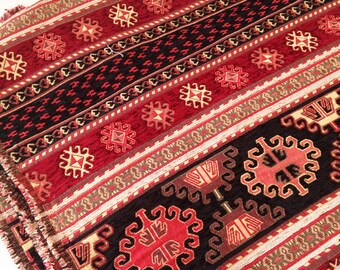 May include: A woven fabric featuring a repeating pattern of geometric shapes in deep red, black, and cream. The textile displays horizontal bands with intricate diamond motifs and stylized floral elements, finished with a frayed edge fringe.