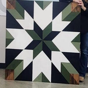 May include: Large, square wooden wall art featuring a geometric star design. The artwork incorporates white, dark green, and black shapes, with wooden corner accents. The star design is centered, creating a striking visual effect.