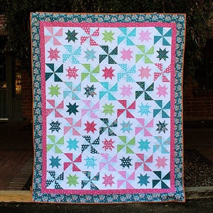 May include: A colourful quilt with a patchwork design featuring a variety of floral and geometric patterns in shades of pink, blue, green, and white. The quilt is bordered with a floral print fabric.