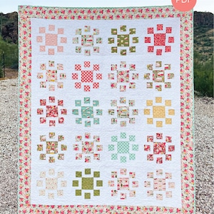 May include: A quilt pattern called "Ensemble" in baby, throw, and twin sizes. The quilt features a floral print with a white background and a variety of colors, including pink, red, green, and blue. The quilt is made up of 12 squares, each with a different pattern. The quilt is surrounded by a floral border. The text "HELLO Melly DESIGNS #133" is printed at the bottom of the quilt.