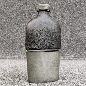 Peut inclure: Une flasque vintage avec un dessus en cuir noir et un fond en métal argenté. La flasque a un petit bouchon argenté. Le cuir a un aspect texturé. La flasque est conçue pour contenir des liquides.