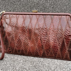 Peut inclure: Une pochette en cuir de serpent brun avec une fermeture à fermoir dorée et une dragonne.
