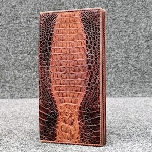 May include: A brown leather wallet with a crocodile skin pattern. The wallet is rectangular and has a vertical orientation. The color of the wallet transitions from a lighter brown at the bottom to a darker brown at the top.