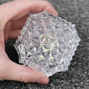 May include: A clear glass trinket box with a geometric pattern. The box is held in a hand.
