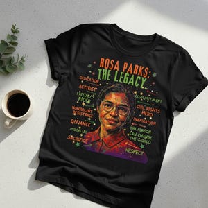 May include: Black t-shirt featuring a portrait of Rosa Parks with the text "ROSA PARKS: THE LEGACY." Additional words include "Dedication," "Activist," and "Civil Rights Hero." The shirt has a crew neck and short sleeves.
