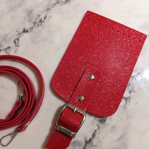 May include: A red glitter leather belt with a silver buckle and a matching red glitter leather strap. The strap is attached to a red glitter leather pouch with silver rivets.