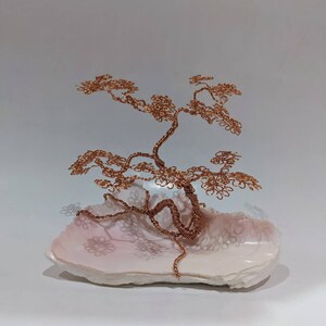 May include: A copper wire bonsai tree sculpture with a delicate, intricate design, resting on a pink seashell base.