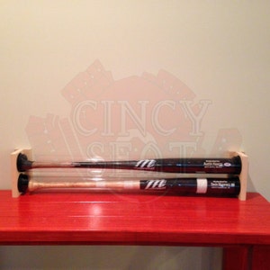 May include: Two baseball bats are displayed in a wooden holder. The bats are encased in clear plastic tubes. The bats are signed by "Austin Kearns" and "Deion Sanders".