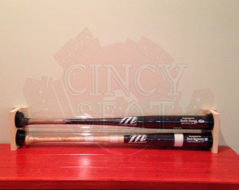 May include: Two baseball bats are displayed in a wooden holder. The bats are encased in clear plastic tubes. The bats are signed by "Austin Kearns" and "Deion Sanders".