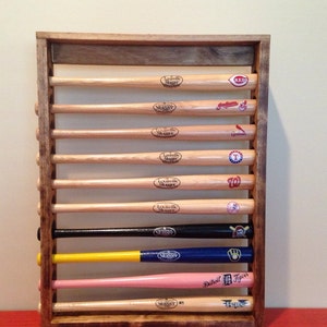 May include: A wooden baseball bat rack with 10 bats displayed. The bats are all Louisville Slugger brand and have different team logos, including the Reds, Indians, Cardinals, Rays, Nationals, Pirates, Brewers, Tigers, and Blue Jays.